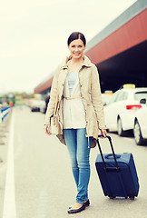 Image showing smiling young woman with travel bag over taxi