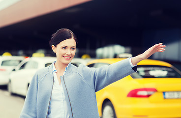 Image showing smiling young woman waving hand and catching taxi