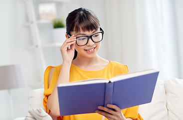 Image showing smiling young asian woman reading book at home