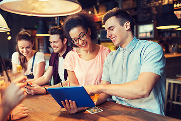 Image showing happy friends with tablet pc and drinks at bar