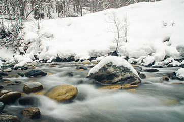 Image showing Rapidly flowing mountain river on a background of snow-covered forest, blurred by a slow shutter speed