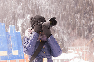 Image showing A young girl takes pictures winter mountain landscape in a snow storm on a SLR camera with telephoto lens