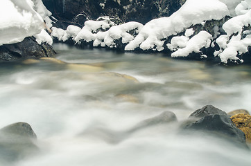 Image showing Mountain river flowing between the rock and snow-covered branches of trees, photographed with a long exposure