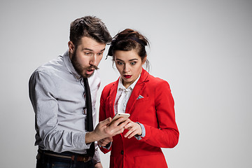 Image showing Business concept. The two young colleagues holding mobile phone on gray background