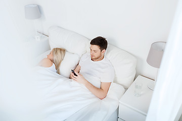 Image showing man texting message while woman is sleeping in bed