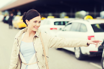 Image showing smiling young woman waving hand and catching taxi