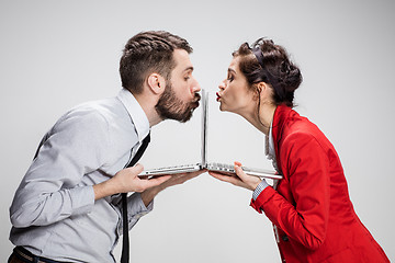 Image showing The young businessman and businesswoman with laptops kissing screens on gray background