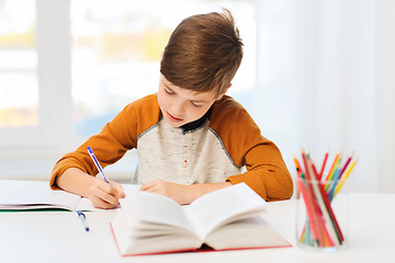 Image showing student boy with book writing to notebook at home