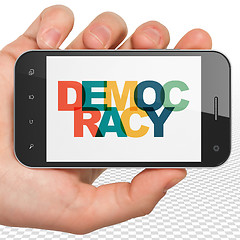 Image showing Politics concept: Hand Holding Smartphone with Democracy on  display