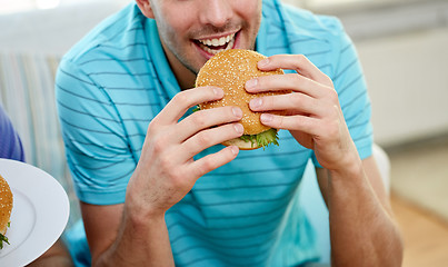 Image showing close up of happy man eating hamburger at home