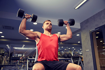 Image showing young man with dumbbells flexing muscles in gym