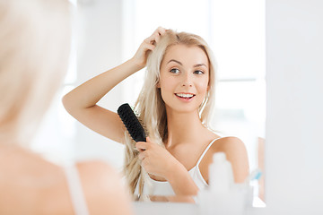 Image showing happy woman brushing hair with comb at bathroom