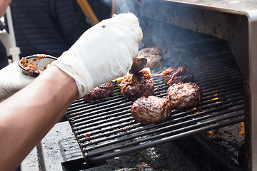 Image showing Beef burgers being grilled on food stall grill.