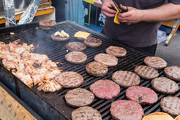 Image showing Beef burgers being grilled on food stall grill.