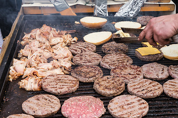 Image showing Beef burgers being grilled on food stall grill.