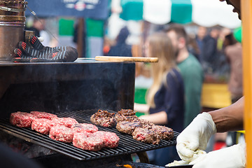 Image showing Beef burgers being grilled on food stall grill.