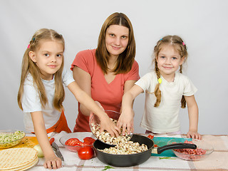 Image showing Two little daughter at the kitchen table helping her mother pour chopped mushrooms from the plate to the pan