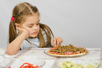 Image showing Little six year old girl sitting at the table and picks unfinished pizza