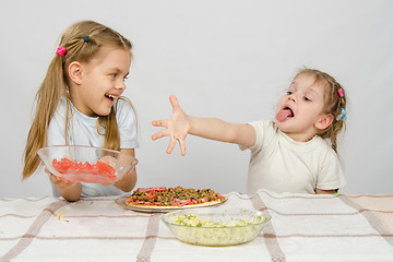 Image showing Two little girls at a table prepared pizza. One with a whimsical view stretches a hand to a plate with tomatoes, which takes the other with a smile