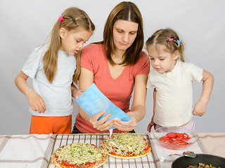 Image showing Two little girls are watching with interest as the mother is watering mayonnaise pizza