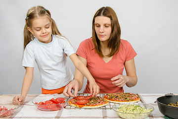 Image showing  Six-year girl helps mother spread on tomato pizza