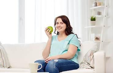 Image showing happy plus size woman eating green apple at home