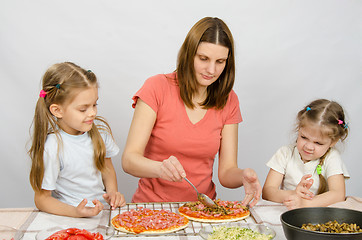 Image showing Two little girls sitting at the kitchen table and watch as a mother preparing a pizza