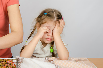 Image showing Little girl wearily rubbing his eyes at the kitchen table while Mom cooks