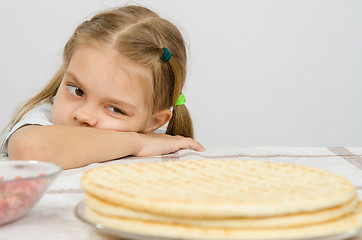 Image showing The girl at the kitchen table laid her head on his hand, and with an appetite for looking at cakes in front of her