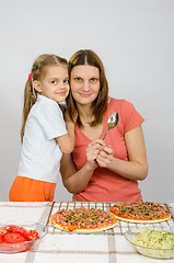 Image showing Daughter hugging her mother six years, which is preparing a pizza