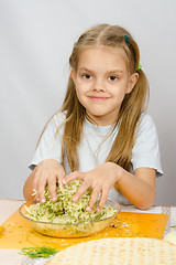 Image showing The girl at the kitchen table with a slight smile mixes hands in a bowl the grated cheese with herbs