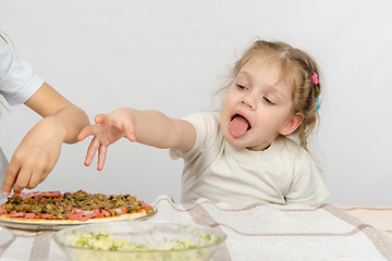 Image showing Little girl with tongue sticking out a hand to pull the pizza, which prepares her older sister