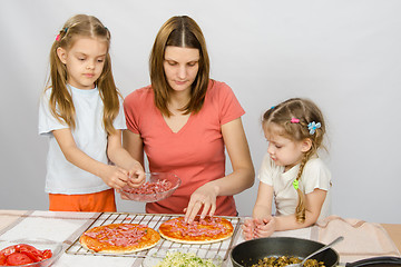 Image showing The eldest daughter helps her mother cook a pizza, and the youngest is watching them