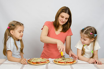 Image showing Mom cuts the pizza, and the two little girls eagerly look