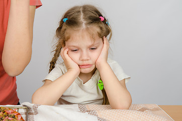 Image showing The baby girl with a sad expression on her face sitting at the kitchen table