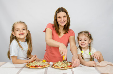Image showing Mother and two little daughters happy sitting at a table with two pizzas