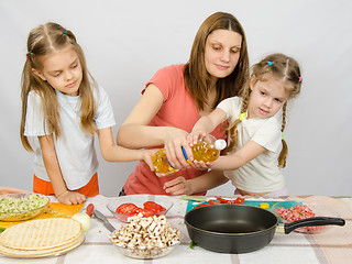 Image showing Two little girls at the kitchen table with enthusiasm to help my mother to pour vegetable oil in a frying pan