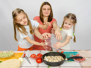 Image showing Mother with two daughters at the kitchen table with a plate of mushrooms is poured into the pan