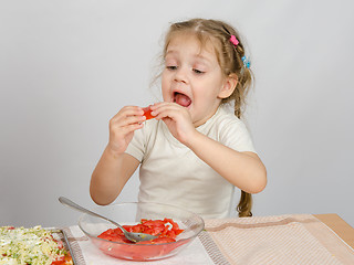 Image showing A little girl tries to stick to widely open mouth large slice of tomato