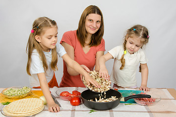 Image showing Two little girls at the kitchen table with a zeal to help her mother pour the mushrooms from the plate to the pan