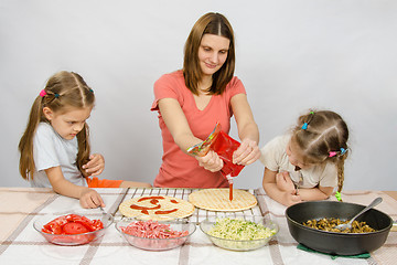 Image showing Two little girls enthusiastically watched as mum pours ketchup basis for pizza