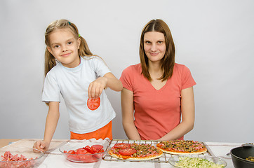 Image showing Six-year girl puts on the pizza tomatoes under the supervision of mum