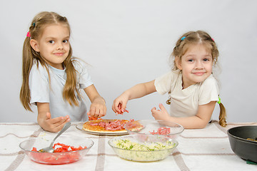 Image showing Two little happy girl at the table spread on the pizza ingredients