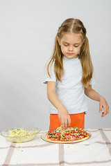 Image showing Little six year old girl standing at the table and sprinkle with grated cheese pizza