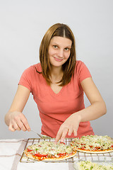 Image showing The girl at the table puts toppings on a pizza with a satisfied look on his face