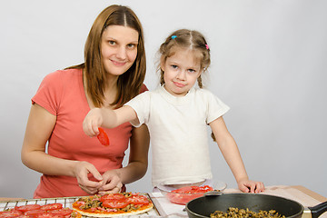 Image showing Little five-year girl helps mother spread on the pizza ingredients