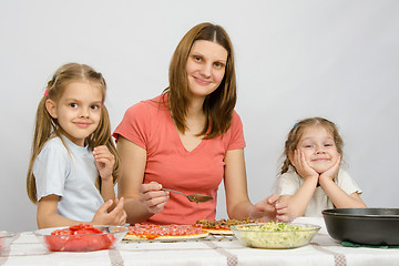 Image showing Mum with two little girls sitting at the kitchen table preparing a pizza