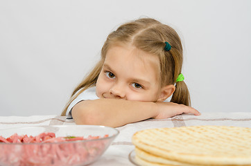 Image showing Little girl sitting at a table with his head on his hand with a smile and looking at the food in front of her