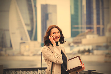 Image showing smiling middle-aged woman with notebook talking on the phone