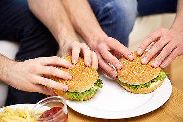 Image showing close up of male hands with hamburgers on table